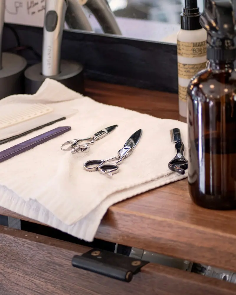 Hair-cutting scissors and a razor laid out on a folded towel at a styling station