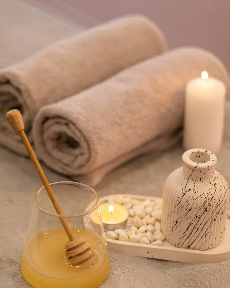 Rolled spa towels, a lit candle and a small glass of honey on a wooden tray